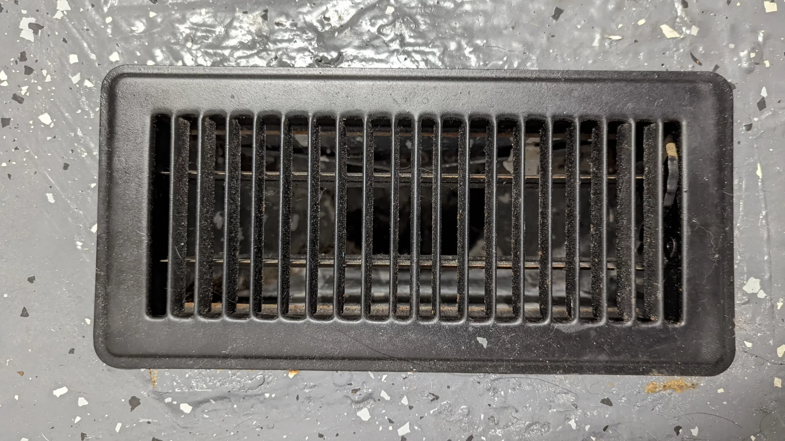 A floor air vent with visible dust and pet hair collected inside